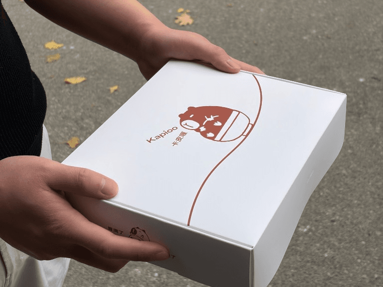 Hands presenting a white Kapioo branded meal box for delivery